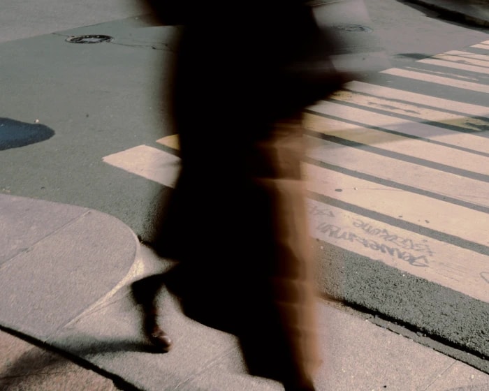 A blurred figure walking across a sunlit pavement