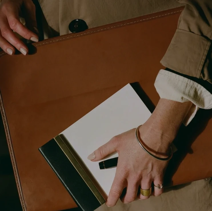 Hands sliding a notebook into a tan leather folio