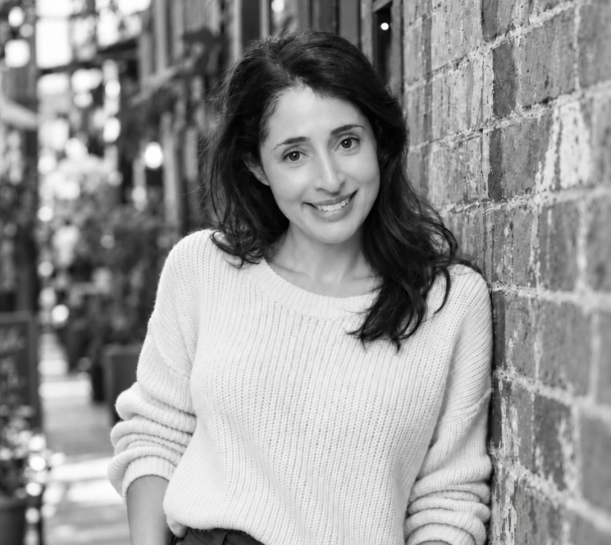 Smiling woman with dark shoulder-length hair wearing a pink knitted jumper with a red heart.
